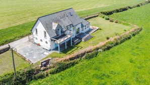 A white house with a grey roof, a balcony, and a paved driveway.