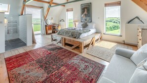 A bedroom with a lofted ceiling, a bed, a desk, and a view of the outdoors.