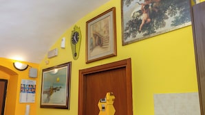 Egy sárga falú szoba, melyben egy fa ajtó, egy képkeretbe foglalt híd, egy képkeretbe foglalt angyalkák és egy a falra szerelt óra található.