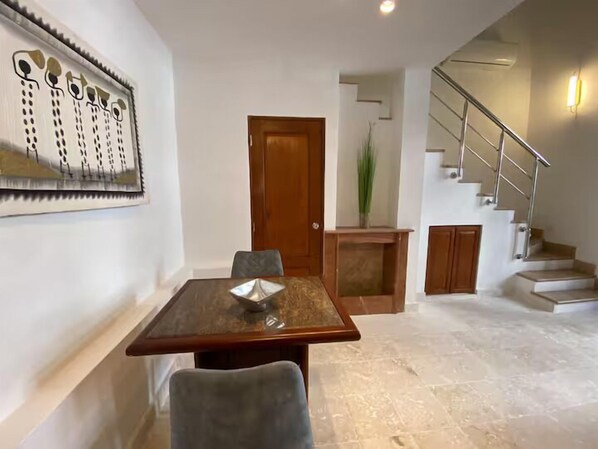 A dining area with a wooden table and chairs, a wooden door, a staircase, and a wall-mounted artwork. - Paseo Colonial - Sanctuary 2 (Santo Domingo)