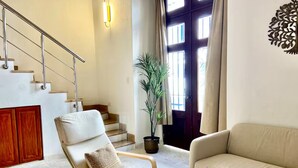 Una sala de estar con un sofá, una silla, una mesita de centro, una planta en maceta y una escalera.