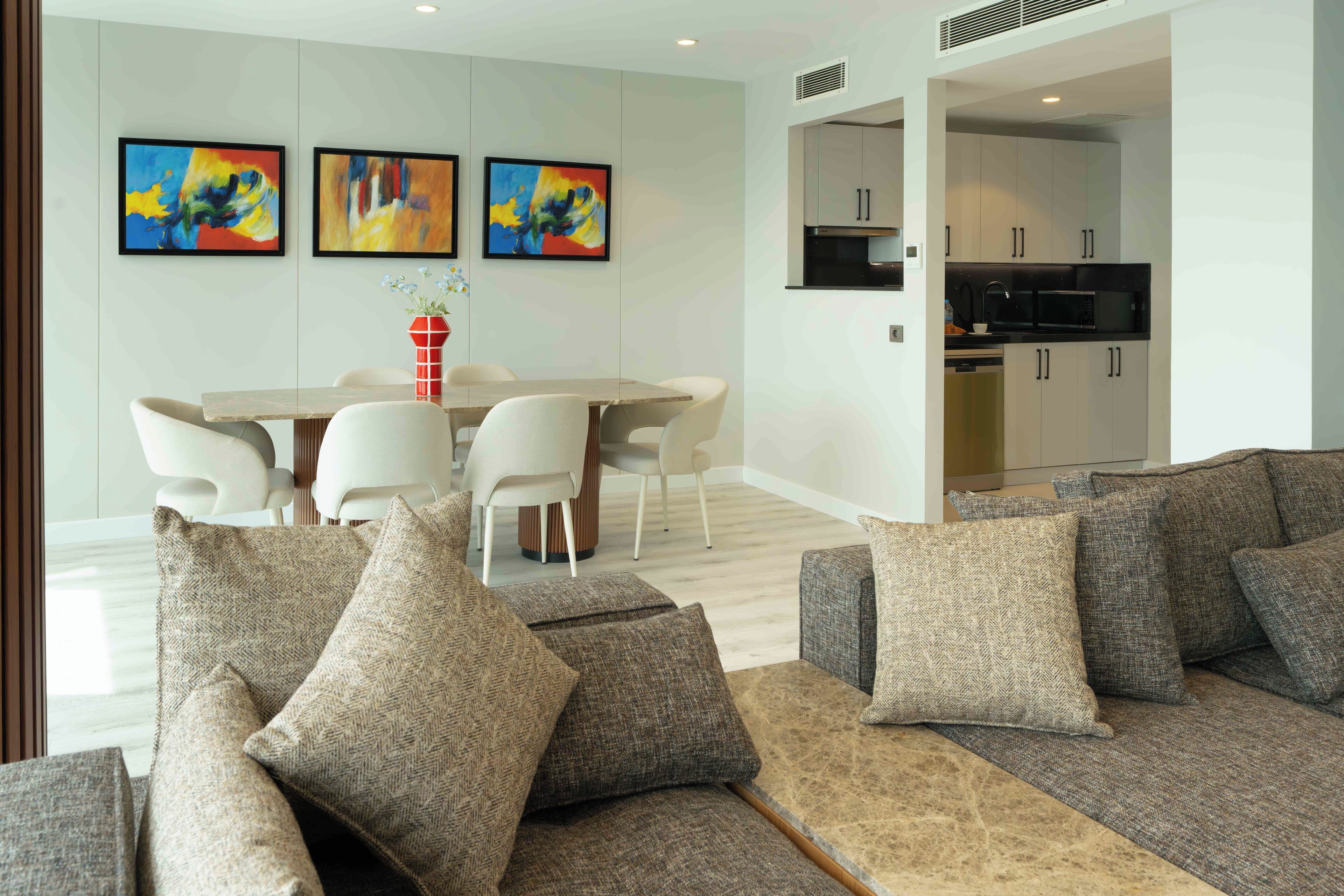 A modern living room with a sofa set, a dining table with chairs, and a kitchen area visible through an open doorway.