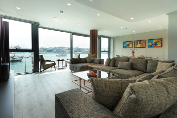 A spacious living room with a large sectional sofa, a glass coffee table, and a view of a body of water through large windows.