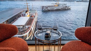 Vista desde una habitación con una mesa dispuesta con dos copas de vino y una botella, con vistas a un cuerpo de agua y barcos.