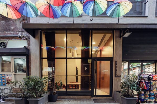 A storefront with large glass windows, a wooden bench outside, and colorful umbrellas above. - DeCamondo Residence Karaköy (Istanbul)