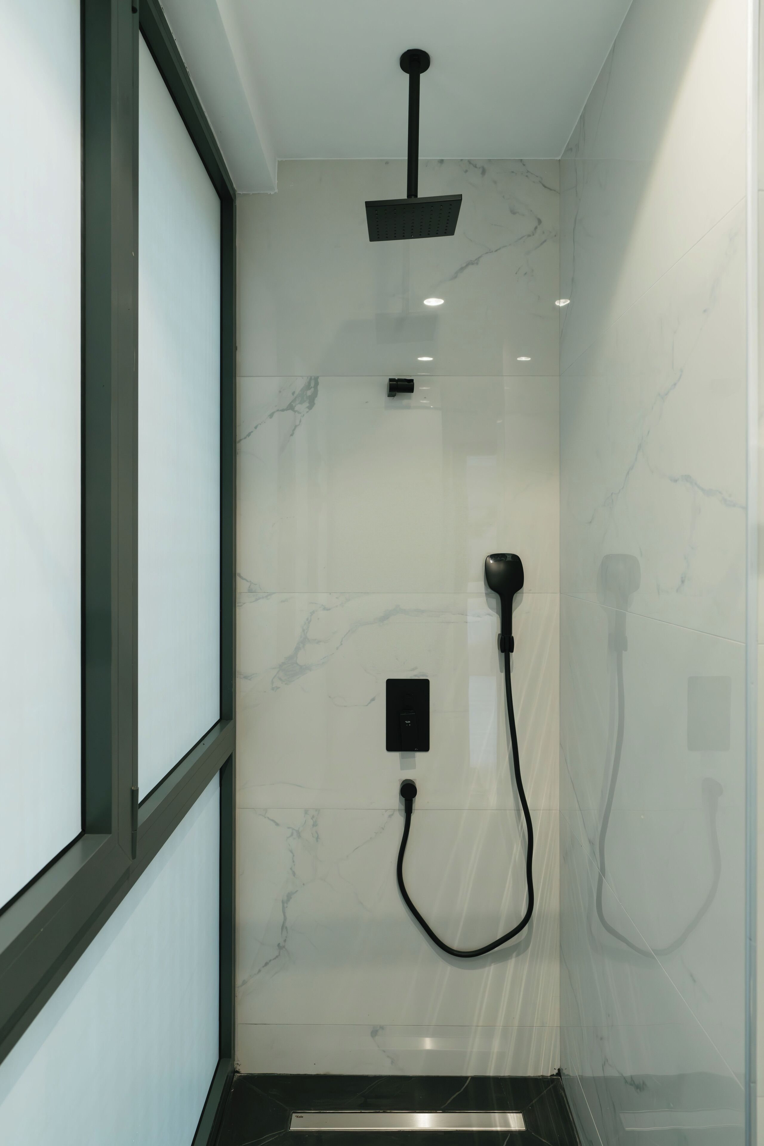 A modern shower with a handheld showerhead and a fixed overhead showerhead, both mounted on a marble wall.