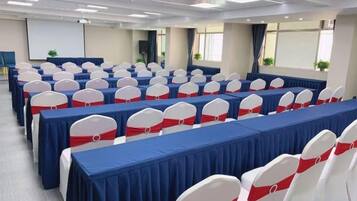 A conference room with rows of tables and chairs, a projector screen, and a large window.