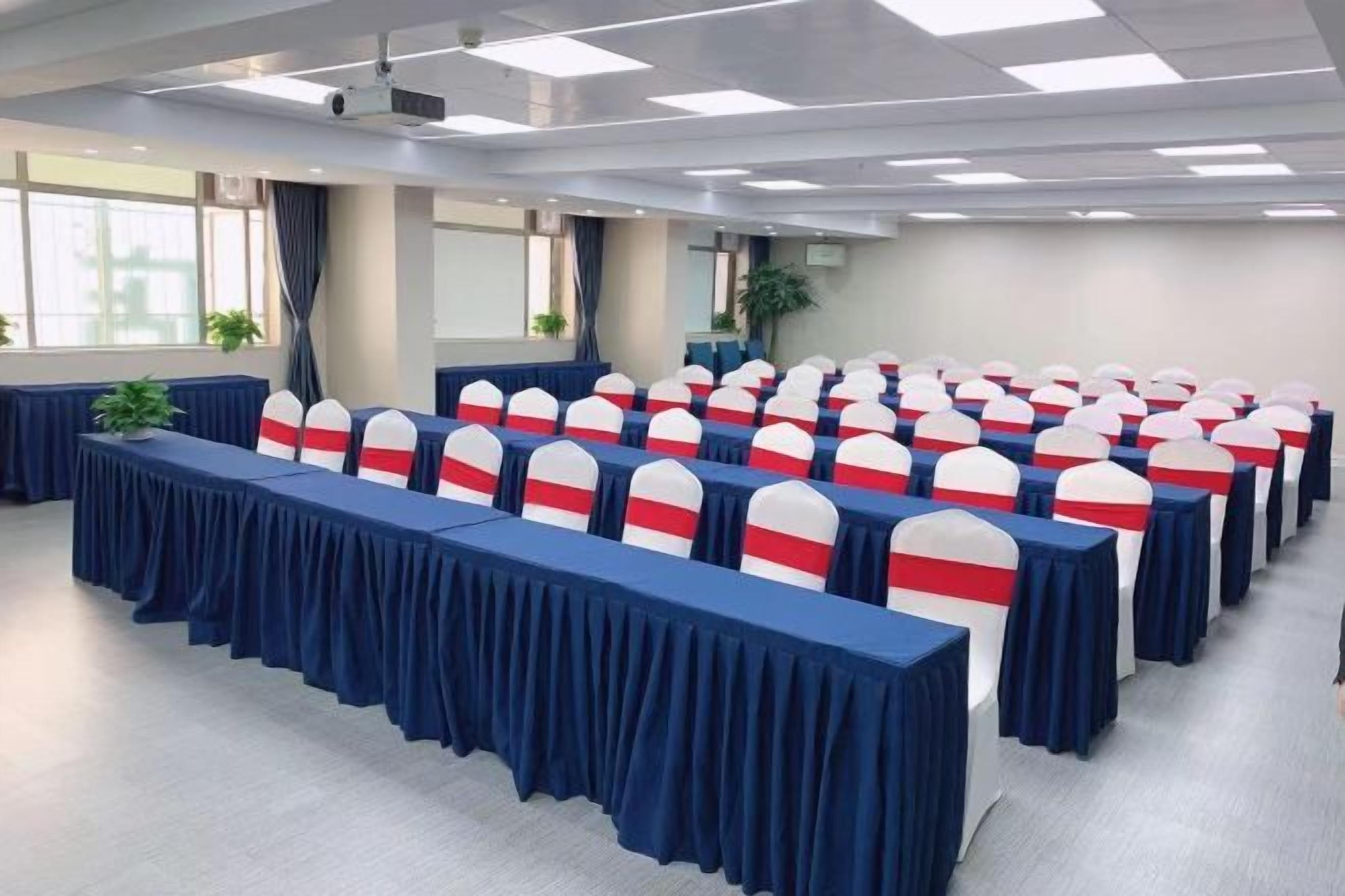 A conference room with rows of tables, chairs, and a projector on the ceiling.