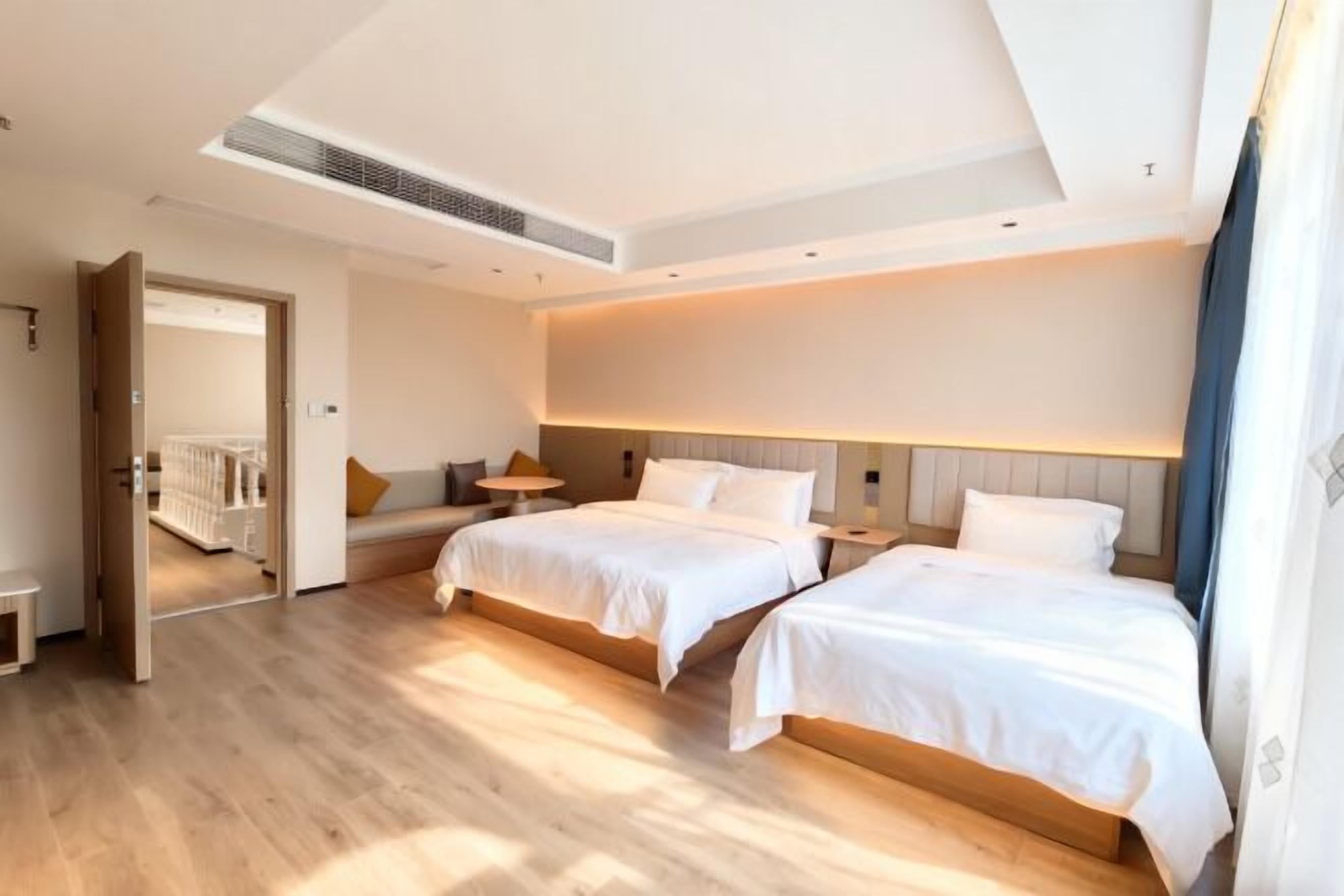 Una camera d'albergo moderna con due letti, una zona relax e vista sul corridoio.