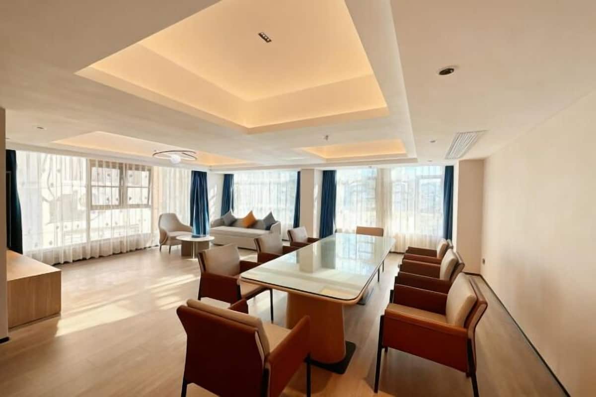 A modern hotel room with a large glass table, comfortable seating, a sofa, and large windows with curtains.