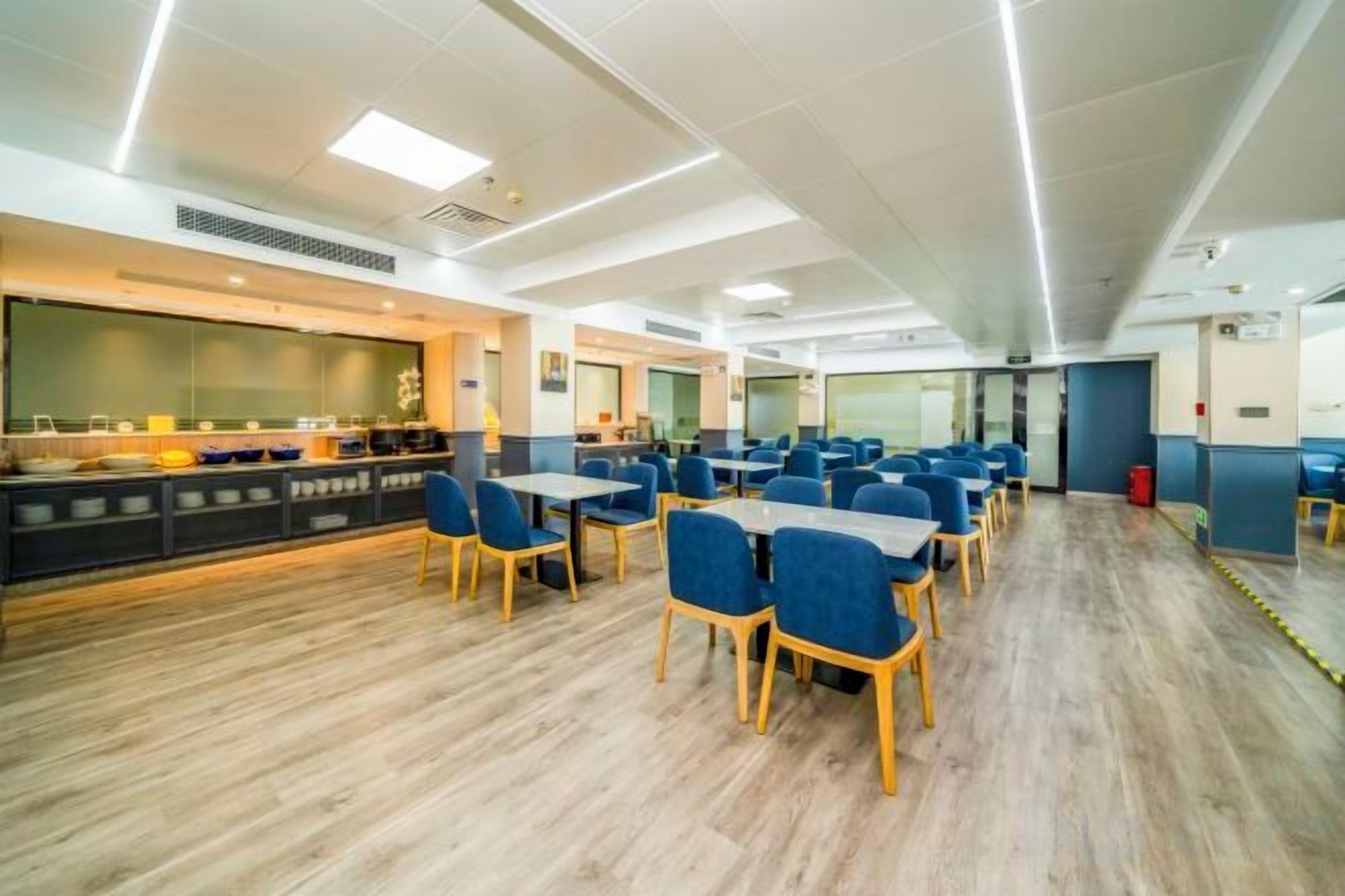 A spacious dining area with multiple tables and chairs, a buffet counter, and a large window providing natural light.