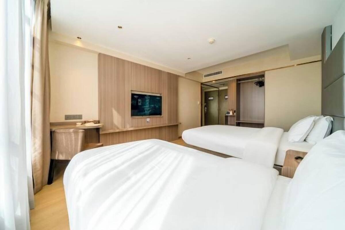 A hotel room with two beds, a TV, a small table, and a mirror.