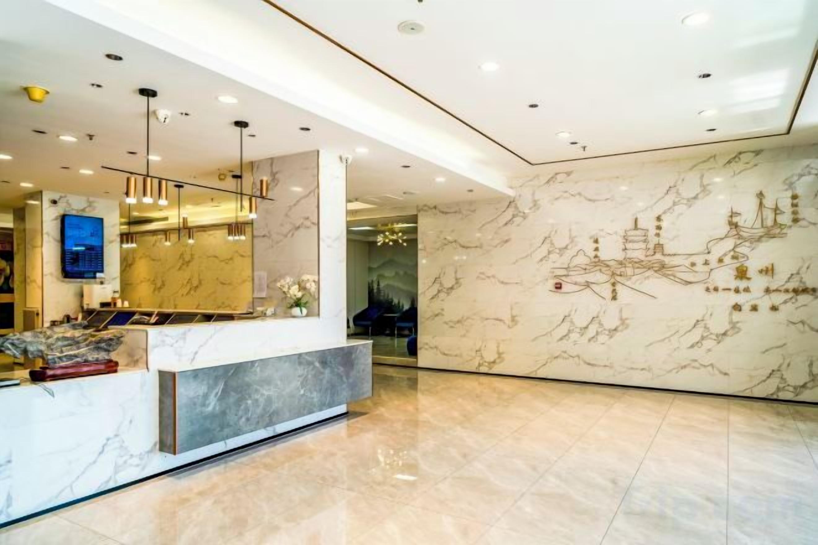 A hotel reception area with a marble reception desk, modern lighting fixtures, and a wall with traditional artwork.