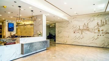 A hotel reception area with a marble reception desk, modern lighting fixtures, and a wall with traditional artwork.