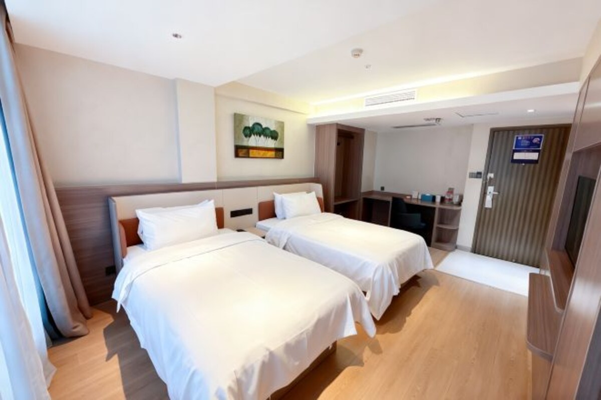 A hotel room with two beds, a desk, a chair, and a door.