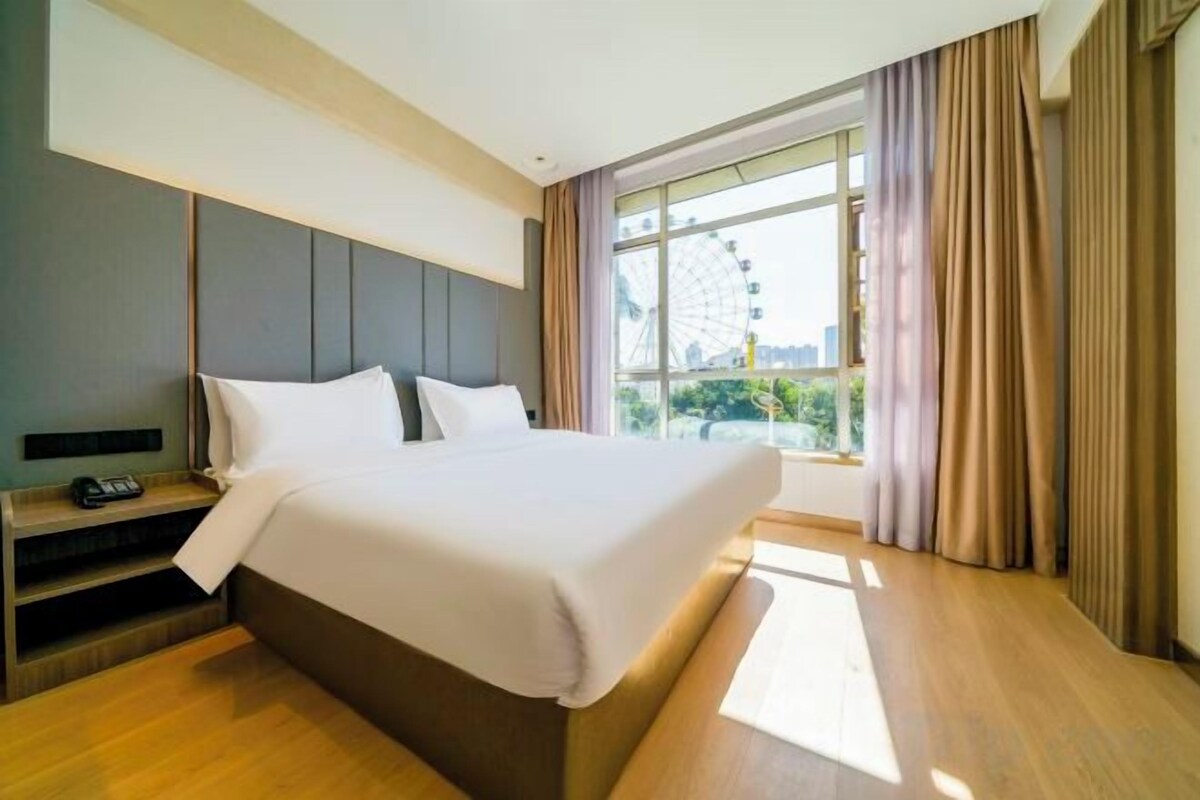 A hotel room with a large bed, a bedside table with a phone, and a window with curtains.