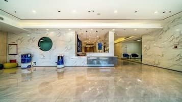 A modern hotel lobby with a marble reception desk, a large mirror, and a clean, polished floor.