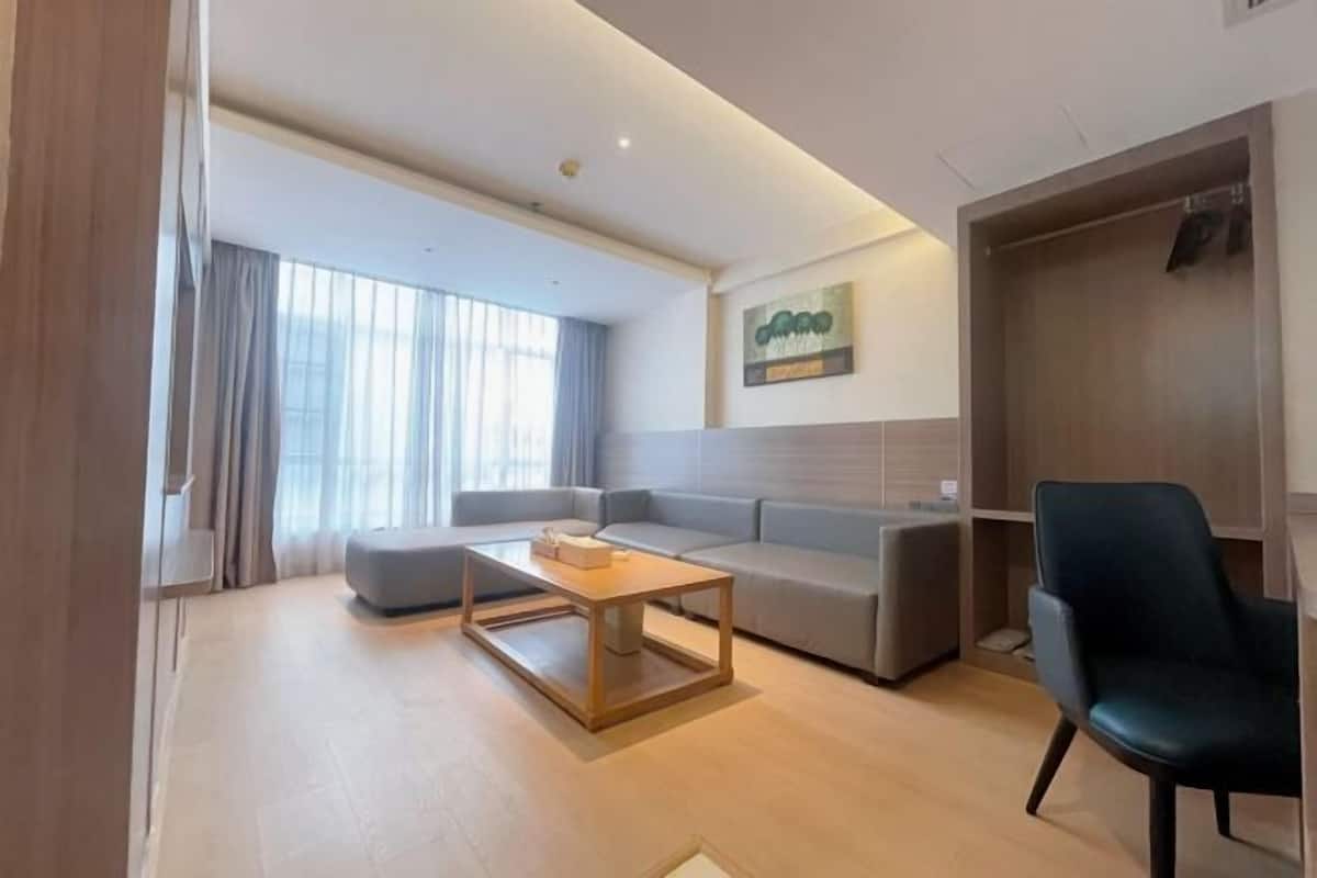 A modern living room with a sofa, a coffee table, and a chair. There is a wardrobe and a painting on the wall.