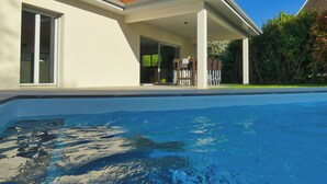 Ett modernt hus med en swimmingpool, en täckt uteplats och en trädgård.