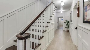 Eine Treppe mit weißen Geländern und einem Holzhandlauf, die zu einem Flur mit hellem Bodenbelag und einem Topfpflanzen führt.