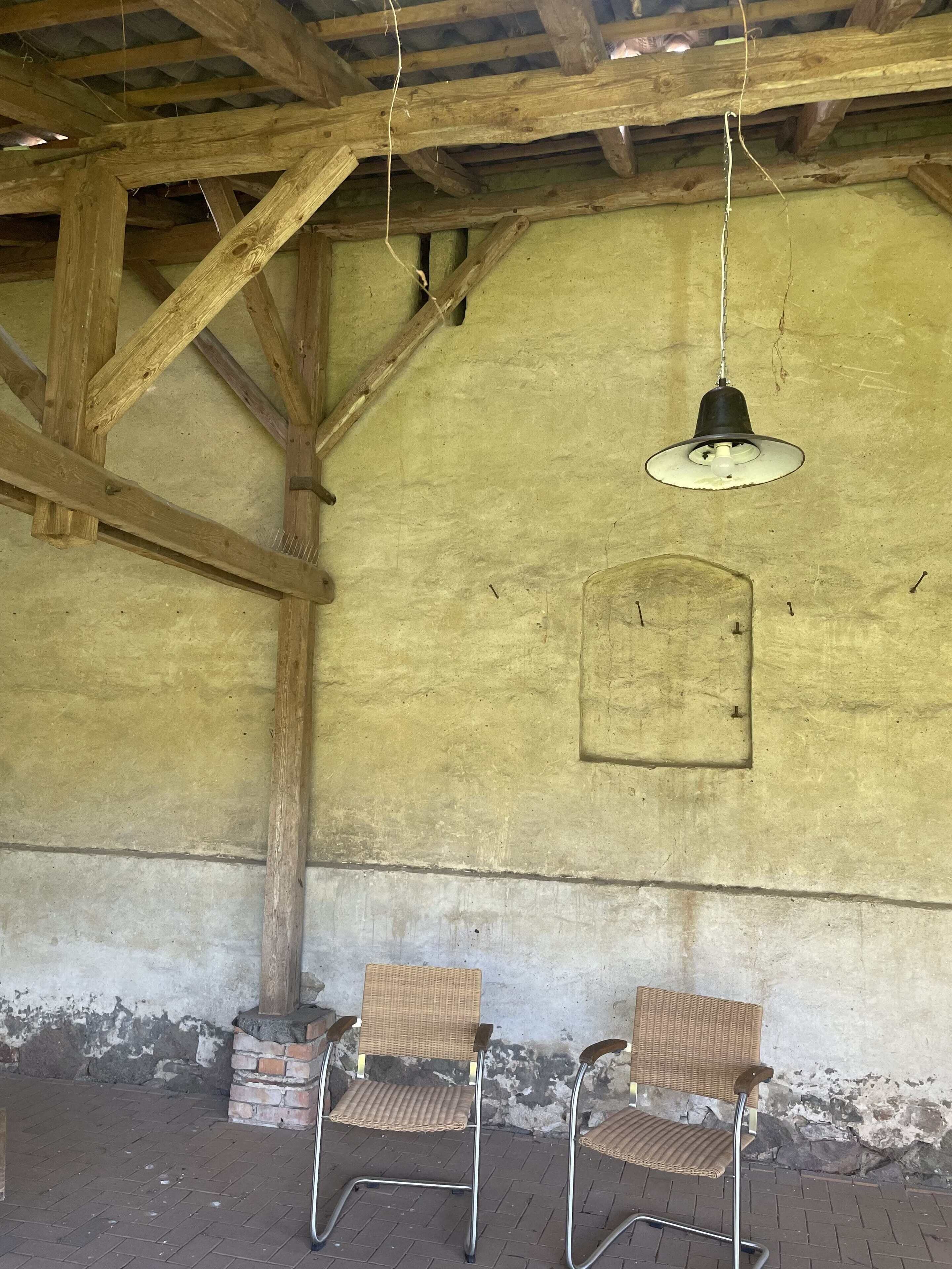 Ein Innenraum mit Holzbalken, einer Hängelampe und zwei Korbstühlen.