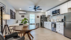 Eine moderne Küche mit weißen Schränken, einem Edelstahlkühlschrank, einer Mikrowelle und einem Backofen. Es gibt einen Esstisch mit Stühlen und einen Deckenventilator.