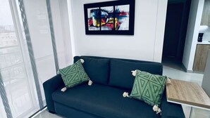A modern living room with a dark sofa, a framed abstract painting, and a small wooden side table.