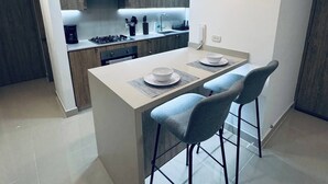 A modern kitchen with a central island, two bar stools, and a wall-mounted clock.