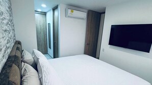 A bedroom with a bed, a sofa, an air conditioning unit, and a TV mounted on the wall.
