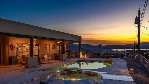 Ein modernes Haus mit Swimmingpool, Sitzgelegenheiten im Freien und Blick auf den Sonnenuntergang.