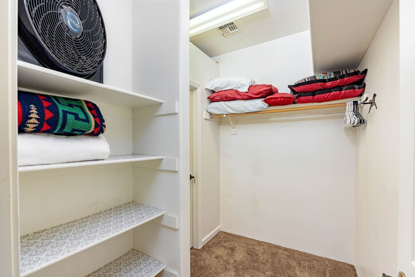 Ein schmaler, kleiner Flur mit einem Schrank, der Regale mit gefalteten Decken und ein Bett mit ordentlich gestapelten Kissen beherbergt.