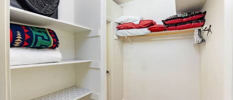 Ein schmaler, kleiner Flur mit einem Schrank, der Regale mit gefalteten Decken und ein Bett mit ordentlich gestapelten Kissen beherbergt.