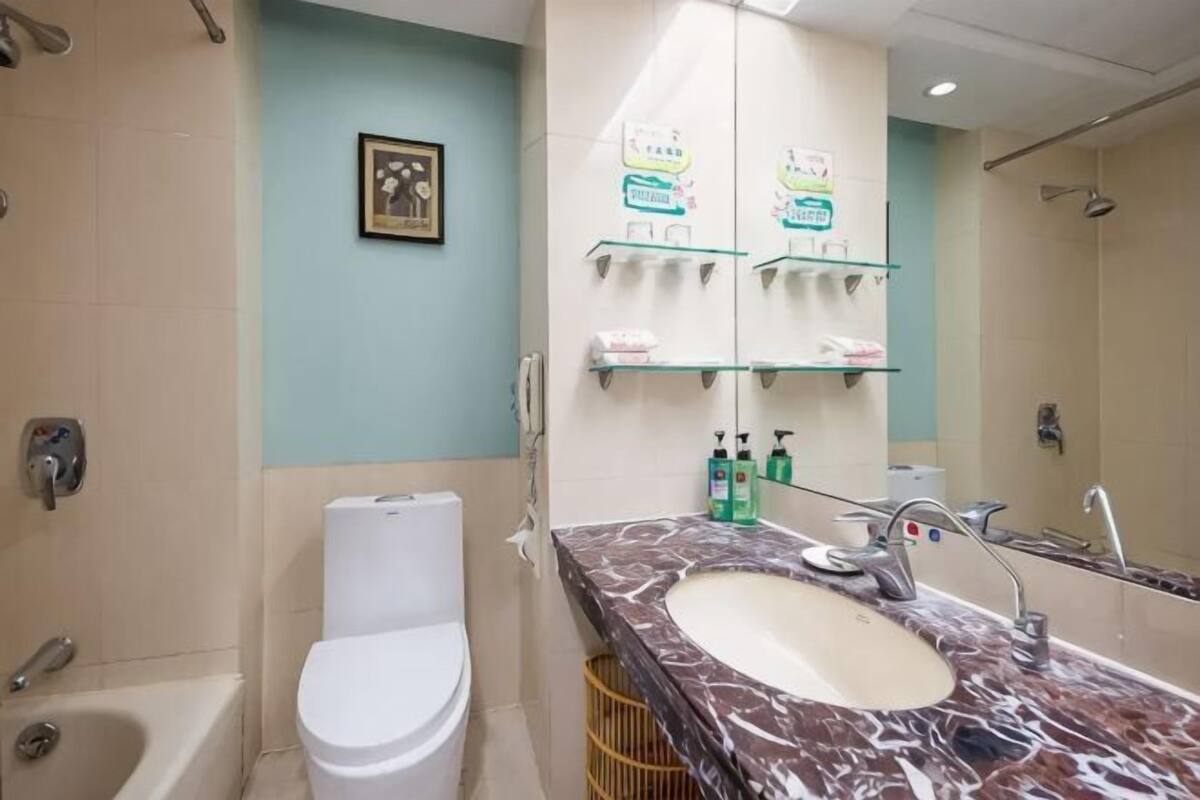 A bathroom with a toilet, sink, mirror, and shelves with toiletries.
