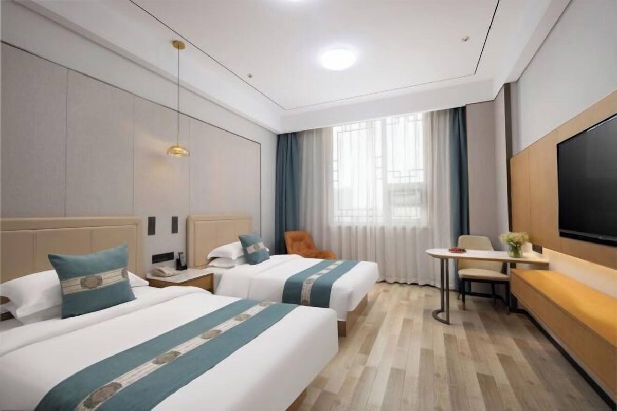 A hotel room with two beds, a desk, a chair, a TV, and a window with curtains.