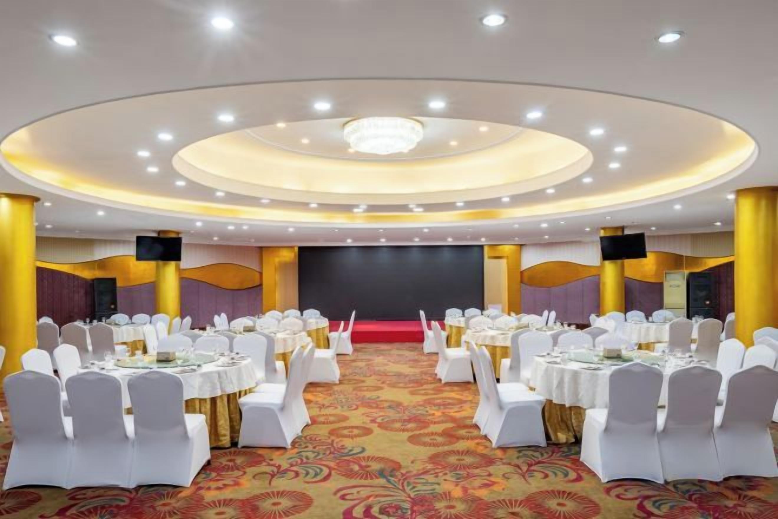 A banquet hall with round tables, white chairs, and a stage.