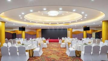 A banquet hall with round tables, white chairs, and a stage.