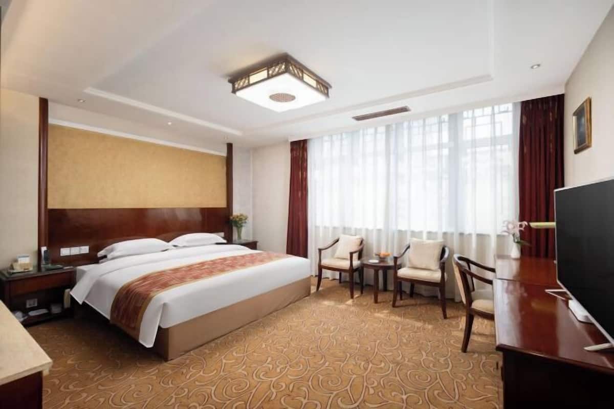 A hotel room with a large bed, a desk, a chair, and a TV.