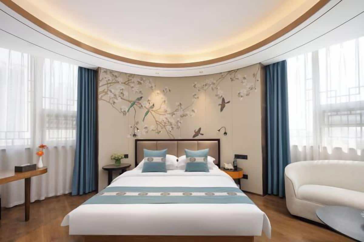 A hotel room with a large bed, a nightstand, a sofa, and a wall with a floral mural.