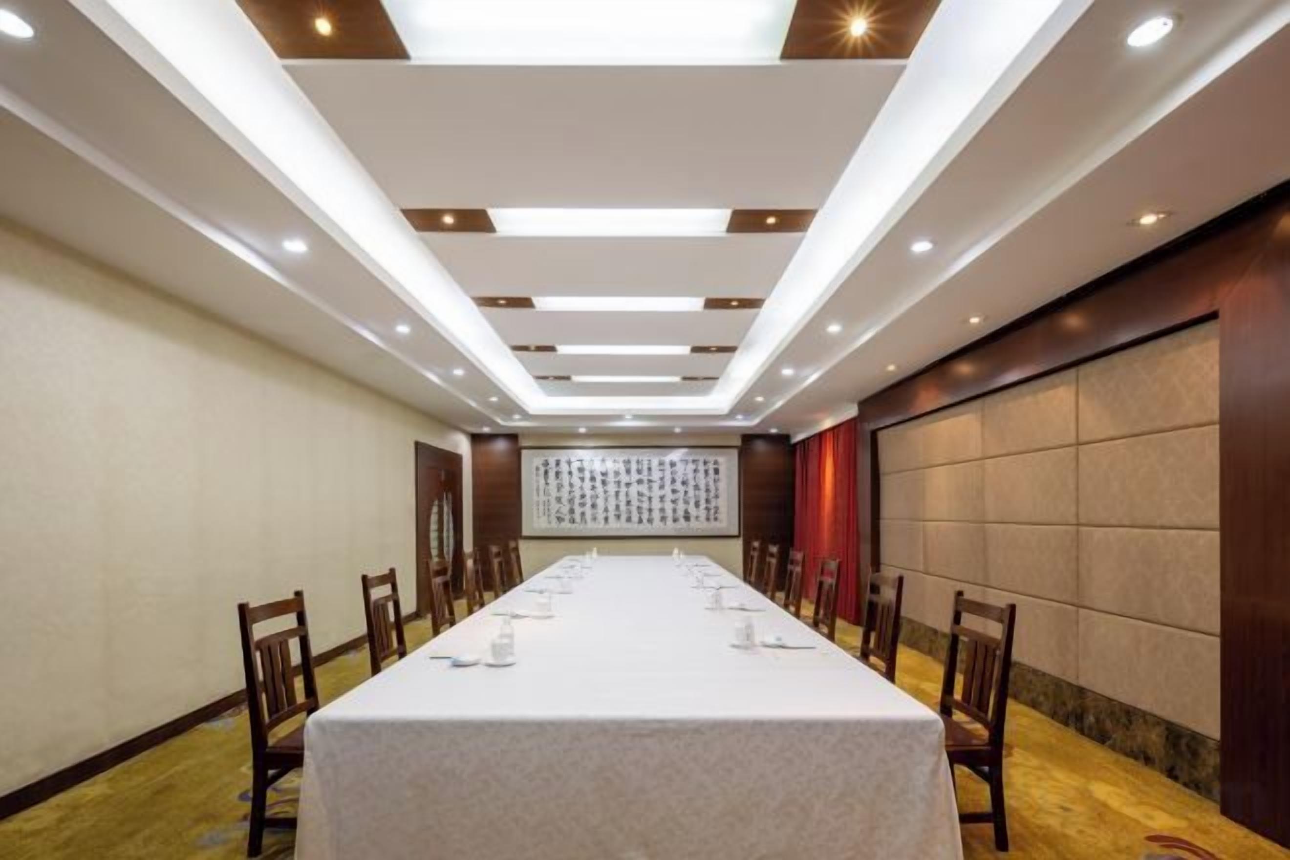 A conference room with a long table, chairs, and a high ceiling with recessed lighting.