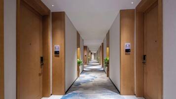 A hotel corridor with wooden doors, a carpeted floor, and a sign indicating the direction to the elevator.