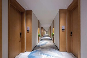Pasillo de hotel con puertas de madera, suelo alfombrado y un letrero que indica el camino al ascensor.