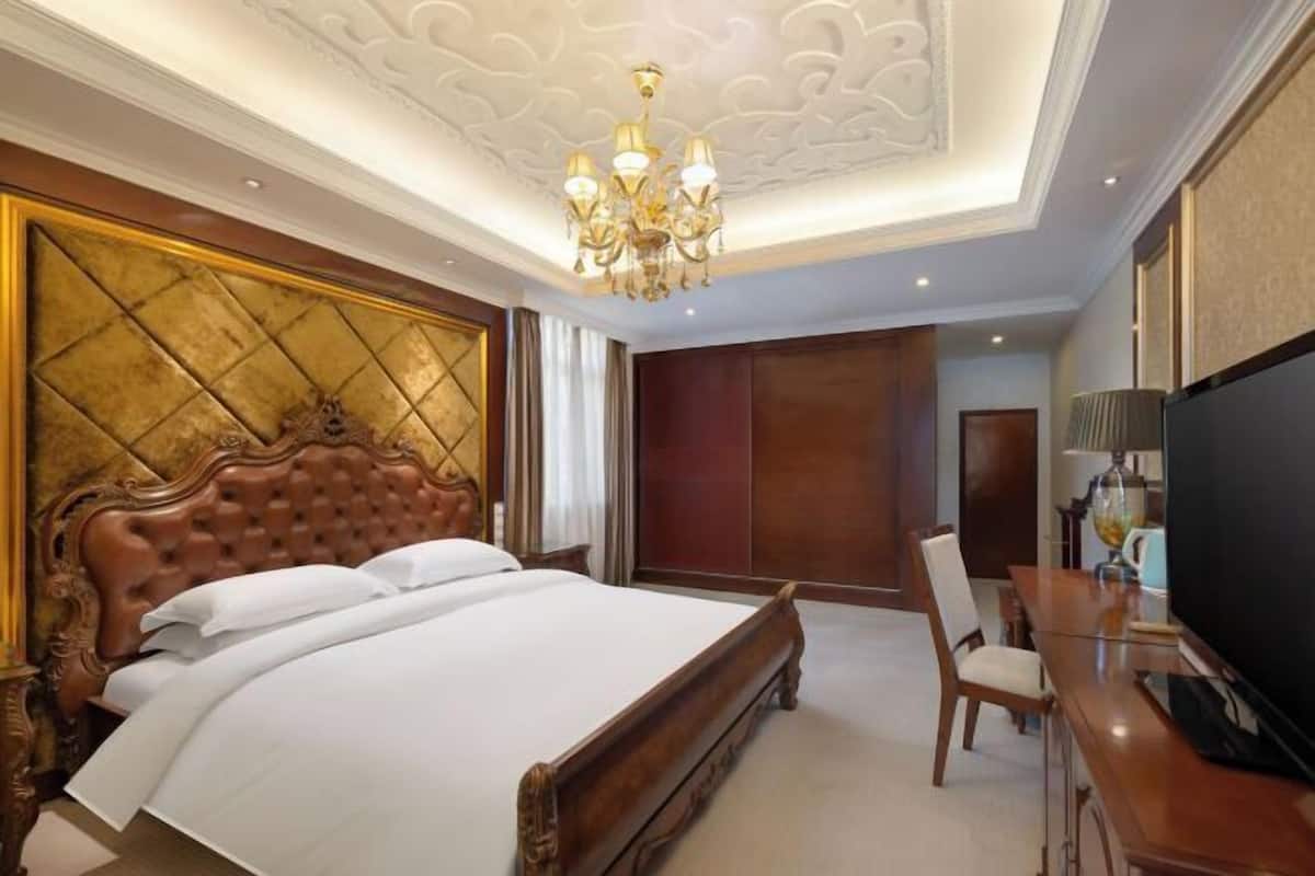A bedroom with a large bed, a chandelier, a television, and a desk.