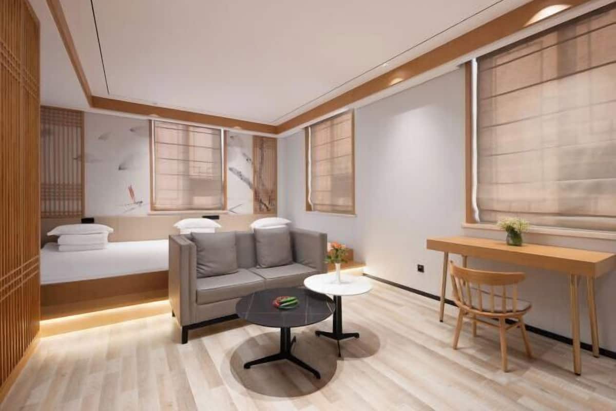 A modern room with a bed, sofa, round table, and wooden desk.
