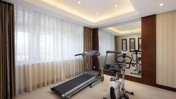 Habitación de hotel con una caminadora, bicicleta estática y ventanas amplias con cortinas.