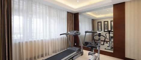 A hotel room with a treadmill, exercise bike, and large windows with curtains.