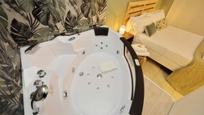 A bathroom with a large bathtub, a wooden headboard, and a white sofa in the adjacent room.