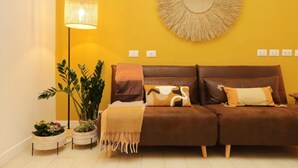 A cozy living room with a brown sofa, a floor lamp, and a round mirror on a yellow wall.