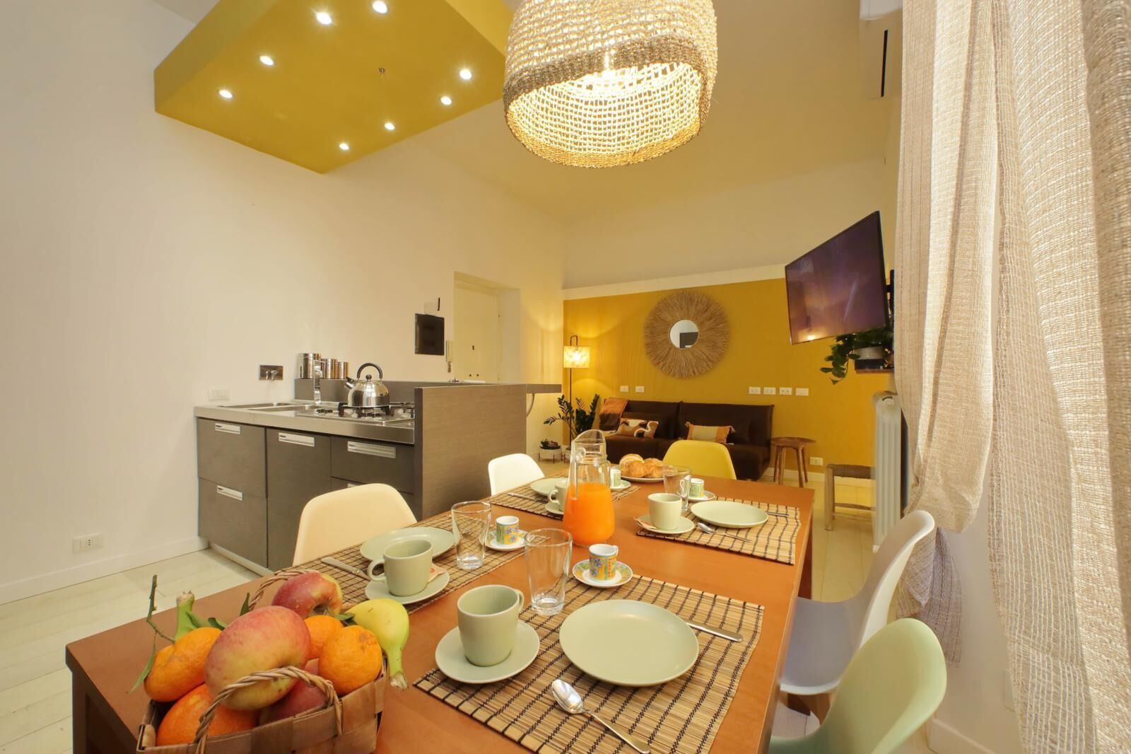 Un espace repas moderne, aménagé pour le petit-déjeuner, avec une table où l’on trouve des assiettes, des tasses et un panier de fruits.