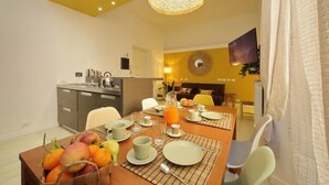 A modern dining area with a breakfast setup, including a table with plates, cups, and a fruit basket.