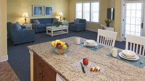 A living room with a blue sofa set, a coffee table, and a dining area with a granite countertop. - RBC 2 Heritage Golf Week 2-BR resort Hilton Head Island - AC, WiFi, fitness room (Hilton Head Island)